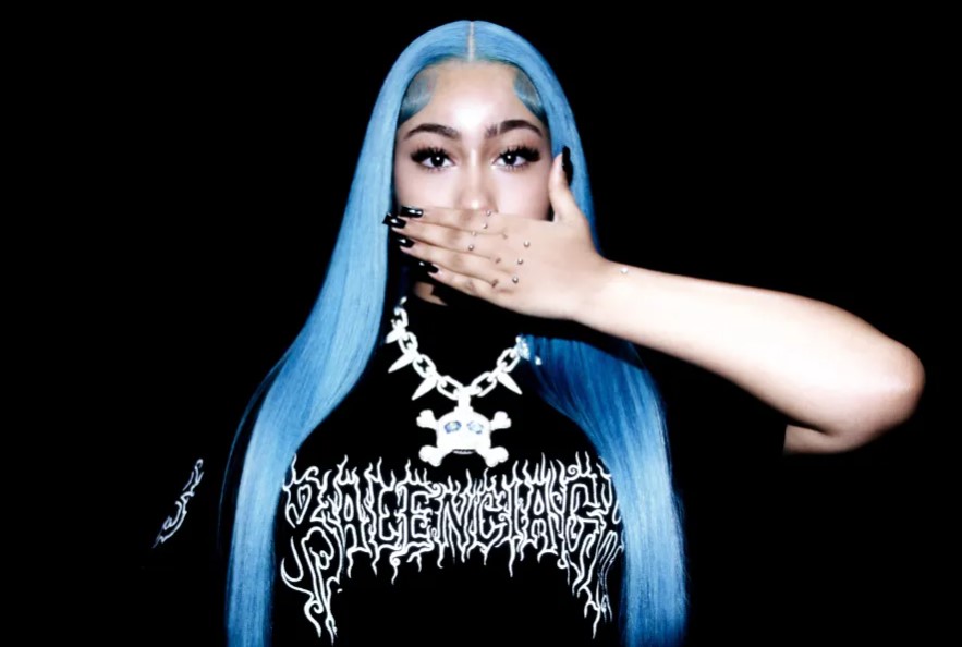 A person with blue hair covering their mouth with their hand, wearing a black shirt with white text.