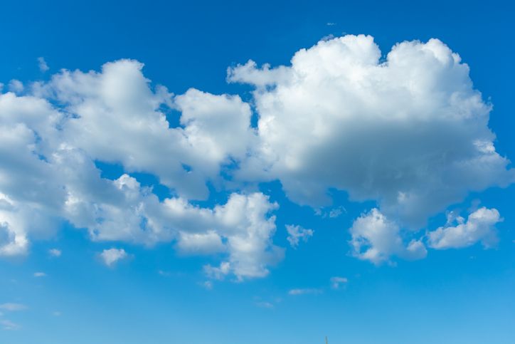 Bright clouds float in a clear blue sky during midday as sunlight shines down on a warm day