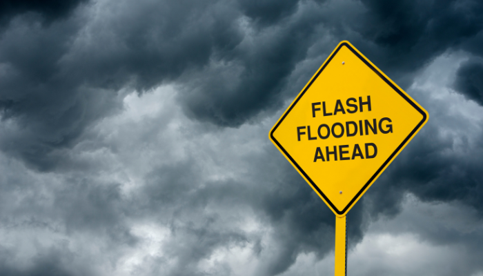 A yellow road sign that says "FLASH FLOODING AHEAD" against a stormy, cloudy sky.