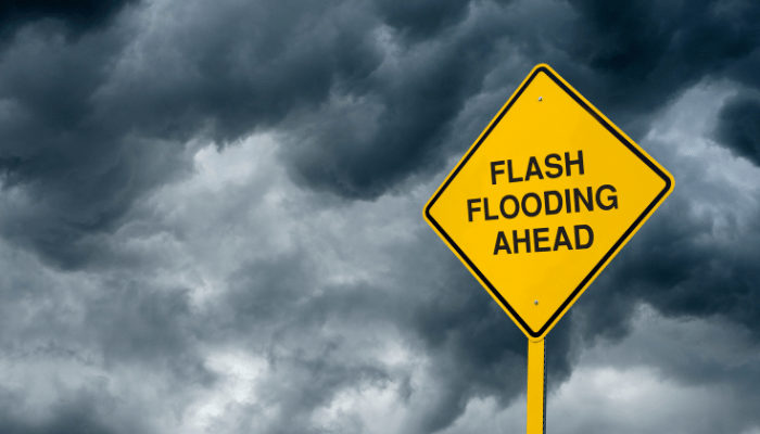 A yellow road sign that says "FLASH FLOODING AHEAD" against a stormy, cloudy sky.